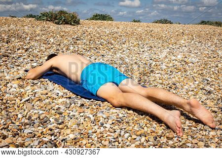 A 18 Year Old Caucasian Shirtless Teenage Boy Sunbathing On A Stoney Beach