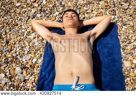 A 18 Year Old Caucasian Shirtless Teenage Boy Sunbathing On A Stoney Beach