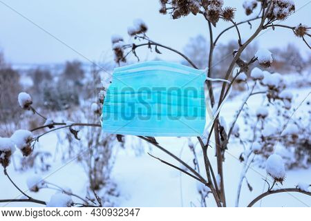 Blue Medical Mask Hanging On Dry Grass Close-up On A Background Of Snow On A Cloudy Day