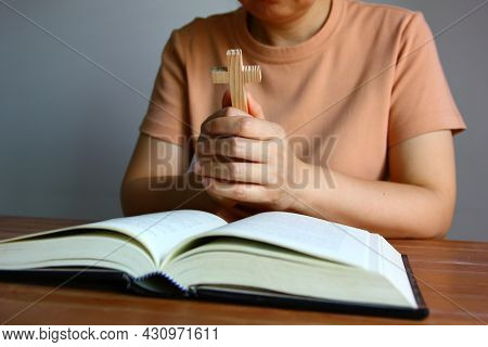 Asian Christain Woman Praying While Holding Wood Cross In Front Of The Bible