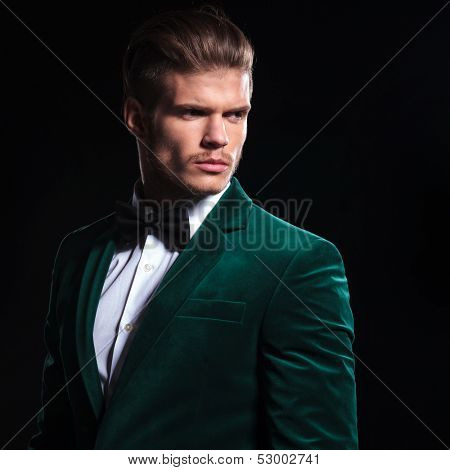 side view of a serious young man in a green velvet suit looking away from the camera on black background