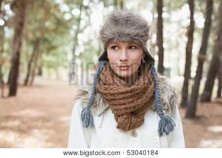 Young beautiful woman wearing fur hat with woolen scarf and jacket in the woods