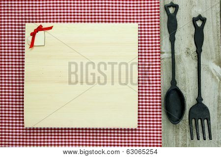 Blank wood menu sign with cast iron spoon and fork on red checkered tablecloth