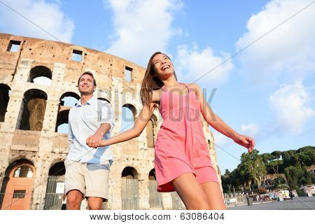 Travel Couple in Rome by Colosseum running fun and romantic holding hands in Italy. Happy lovers on honeymoon sightseeing having fun by Coliseum. Love and travel concept with multiracial couple.