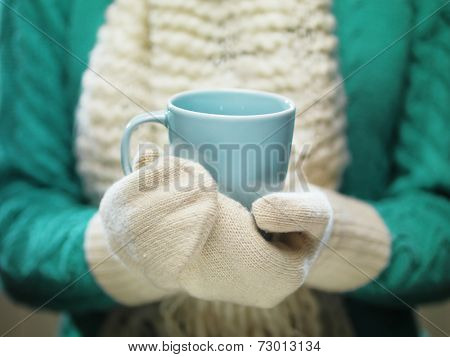 Female hands holding hot mug close up. Woman hands in white woolen mittens holding a cozy cup with hot cocoa, tea or coffee. Winter and Christmas time concept.
