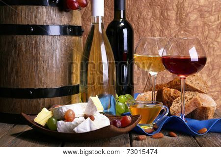 Supper consisting of Camembert and Brie cheese, honey, wine and grapes on napkin in basket and wine barrel on wooden table on brown background