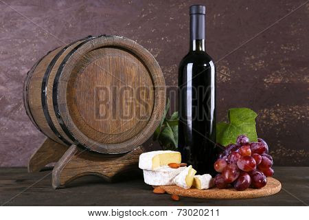 Supper consisting of Camembert cheese, wine and grapes on cutting board and wine barrel on wooden table on brown background