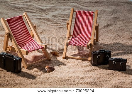 kkleine deck chairs on the sandy beach with suitcase