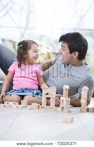Cute girl teasing father while playing with wooden building blocks at home