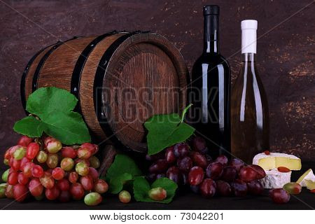 Wine in bottles, Camembert and brie cheese, grapes and wooden barrel on wooden table on wooden background