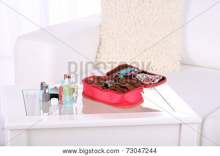 Handbag with accessorises and perfumes in bottles on table on  home interior background