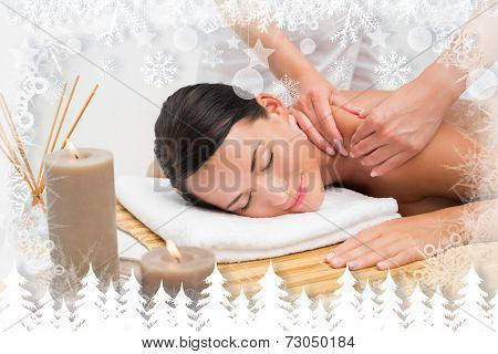Beautiful brunette enjoying a shoulder massage smiling at camera against fir tree forest and snowflakes