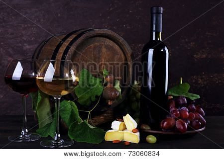 Wine in bottle and in goblets, Camembert cheese, grapes and wooden barrel on wooden table on wooden background