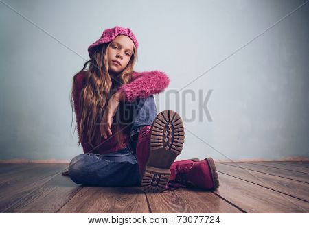 Cute pre-teen girl wearing fashion clothes and shoes sitting on wooden floor
