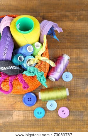 Round orange box full of multicoloured thread and everything necessary for sewing on wooden background