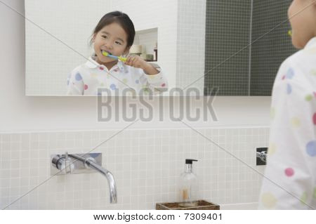 Reflexo da jovem menina pijama, escovando os dentes