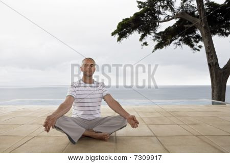 Mand sidder i yoga stilling på terrassen ved infinity-poolen