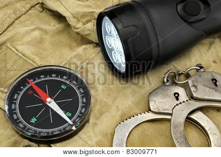 Black Searchlight, Compass And  Handcuffs On Weathered Handbag