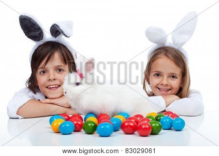 Happy kids at easter time - wearing bunny ears and guarding their white rabbit and colorful eggs