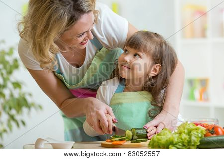 mother and daughter cooking and cutting vegetables on kitchen