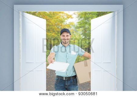 Delivery man with package giving clipboard for signature against scenic shot of narrow road along forest