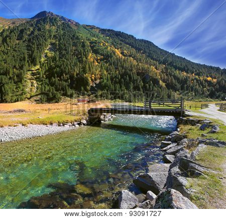 Austrian Alps.  Starting famous Krimml waterfalls. Crystal clear water sparkles in the midday sun. Through the narrow creek wooden bridge spanned