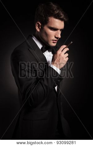 Side view of a elegant young man holding a cigarette in his hand.