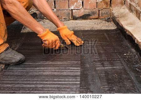 Roofer cut a piece of rolled waterproofing. Professional master making waterproofing. Installation of roll roofing waterproofing propane blowtorch during construction.
