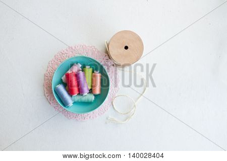 Multi-colored thread bobbins in blue bowl with spool of twine and pink doily