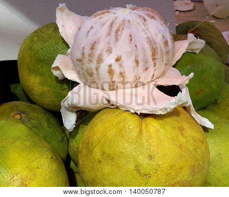 mostly peeled pomelo fruit sitting on top of a stack of unpeeled pomelos for sale at a market, Songkhla, Thailand