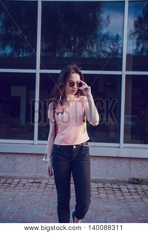 stylish girl walking in the evening city with a phone and a headset