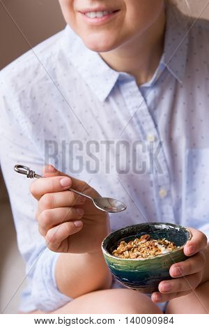 Young woman with muesli bowl. Girl eating breakfast cereals with nuts pumpkin seeds oats and yogurt in bowl. Girl holding homemade granola. Healthy snack or breakfst in the morning.