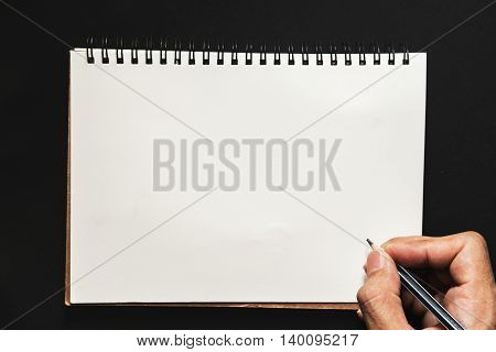 Hand holding pencil writing on scratch paper on black background