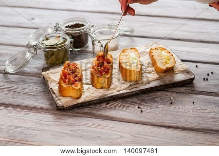 Slices of bread with vegetables. Hand holding long spoon. Recipe of vegetarian bruschetta. Baked tomatoes and eggplant.