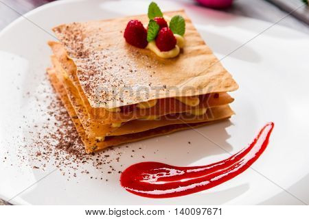 Dessert with fresh raspberries. Red sauce on white plate. Special recipe of millefeuille. Chocolate crumbs and sweet custard.
