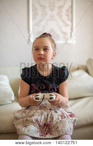 cute little girl sitting on the couch and playing video games with joystick