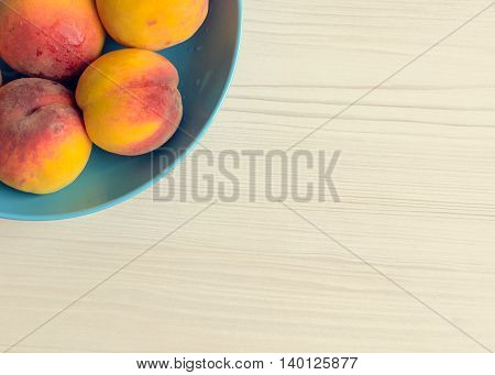 Ripe peaches in blue bowl on white wooden background. Group of fresh peaches on white table. Juicy and fresh peach with place for text. Concept for healthy eating and nutrition. Top view. Copy Space.