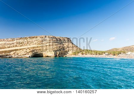 Matala beach on Crete island, Greece. Tourists relax and bath in crystal clear water of Matala in south of Creta. There are many caves near the beach.