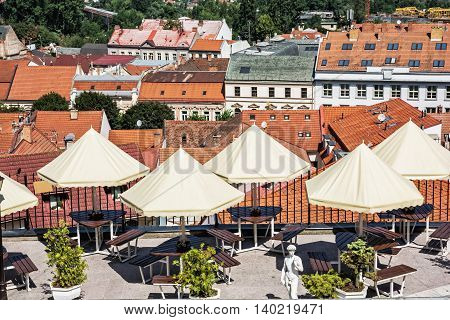 Empty tables chairs and umbrellas in the garden restaurant Trencin city Slovak republic. Red roofs. Urban scene.