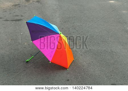 Rainbow umbrella lying on the pavement after the summer rain, forgotten by a child. Sadness and loneliness