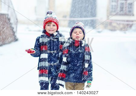 Two little kid boys in colorful clothes, outdoors during snowfall. Active outoors leisure with children in winter on cold snowy days. Happy siblings having fun with snow