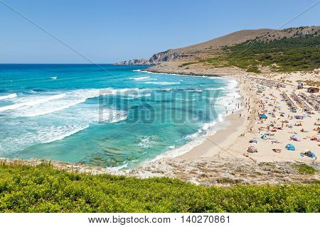 Azure seaboard of Mallorca with peopled beach exciting sea cloudless sky mountains and a riot of greenery.