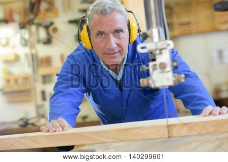 senior carpenter cutting wood with bandsaw in workshop