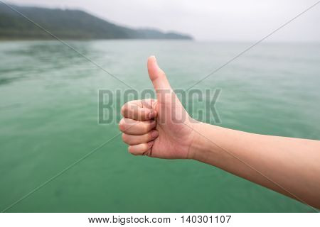 Women hand with thumb up on green sea backgroundsoft focused