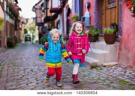 Cute little girl and boy walking down a street in historical medieval city center on cold autumn day. Children during fall vacation in Eguisheim Alsace France. Travelling and tourism with kids.