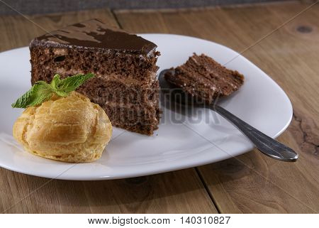 Dessert on a plate on a rustic wooden table: profiterole, decorated with mint leaves and a slice of chocolate cake