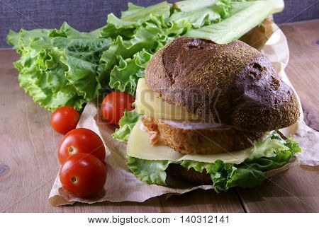 Picnic, sandwich with meat, cheese and fresh vegetables is lying on a rustic wooden table.