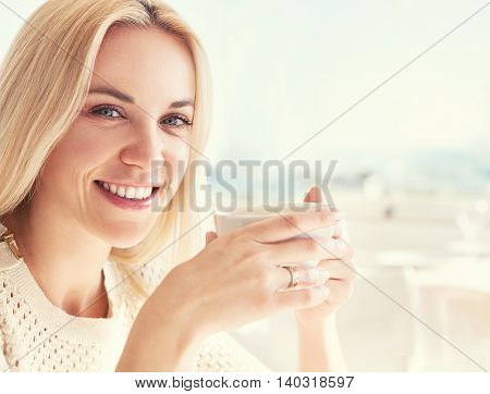 Pretty young woman with cup of coffee in sunny restaraunt