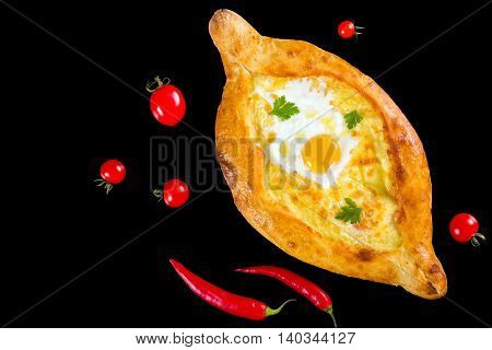 Ajarian khachapuri with egg isolated on black background with cherry tomatoes and red chili pepper authentic recipe view from above