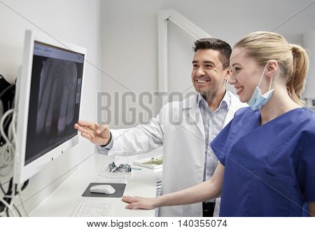 people, medicine, stomatology, technology and health care concept - happy dentists looking to x-ray scan on monitor at dental clinic